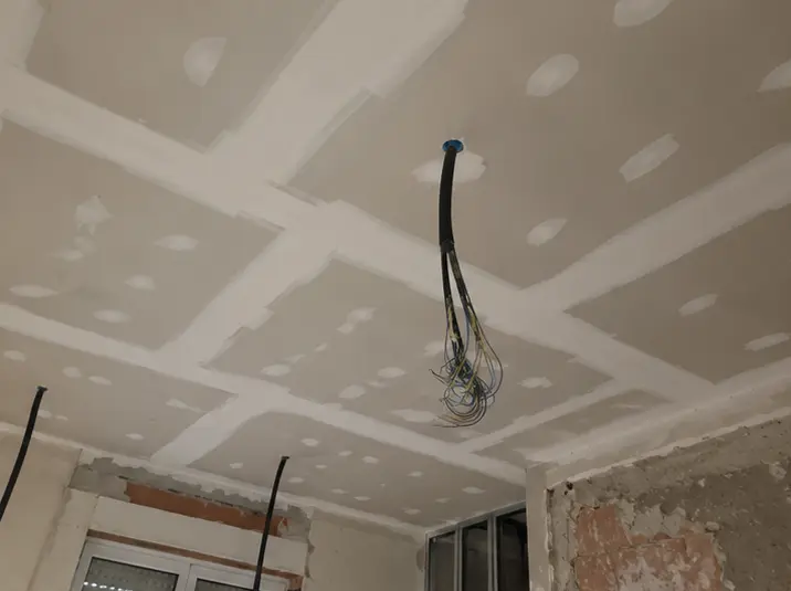 Controsoffitto in cartongesso in posa, con giunti stuccati e cavi elettrici pendenti dal centro.