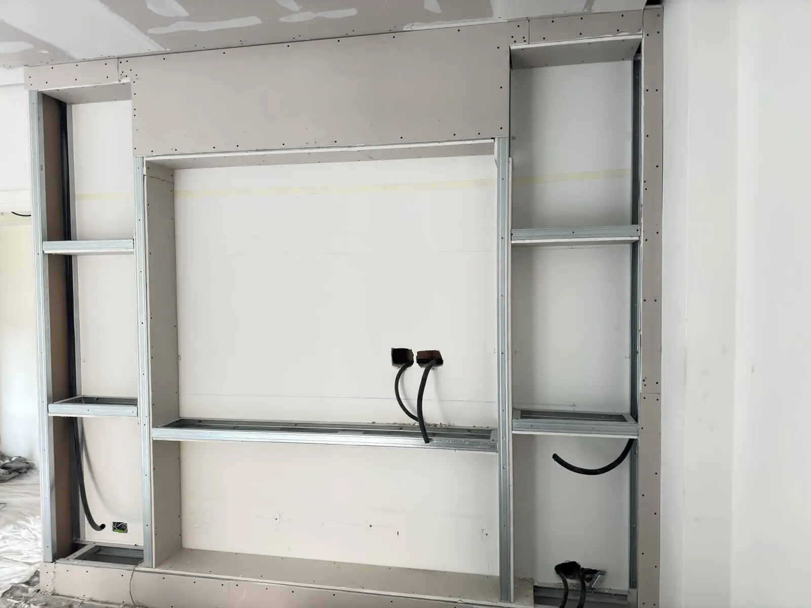 Parete in cartongesso in costruzione con nicchie, profili metallici e canaline elettriche a vista.