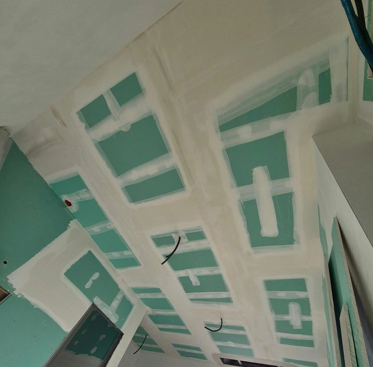 Controsoffitto in cartongesso verde in fase di posa, con giunti stuccati e cavi elettrici pendenti.