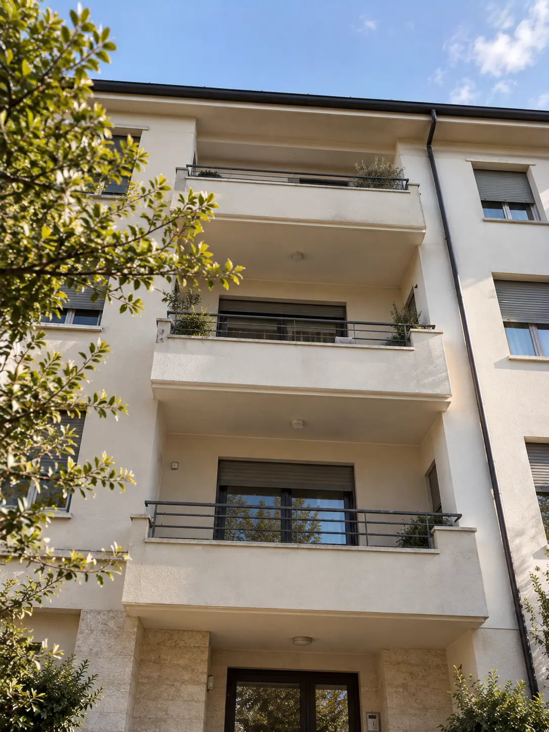 Facciata chiara di un edificio residenziale a più piani con balconi, ringhiere scure e piante.