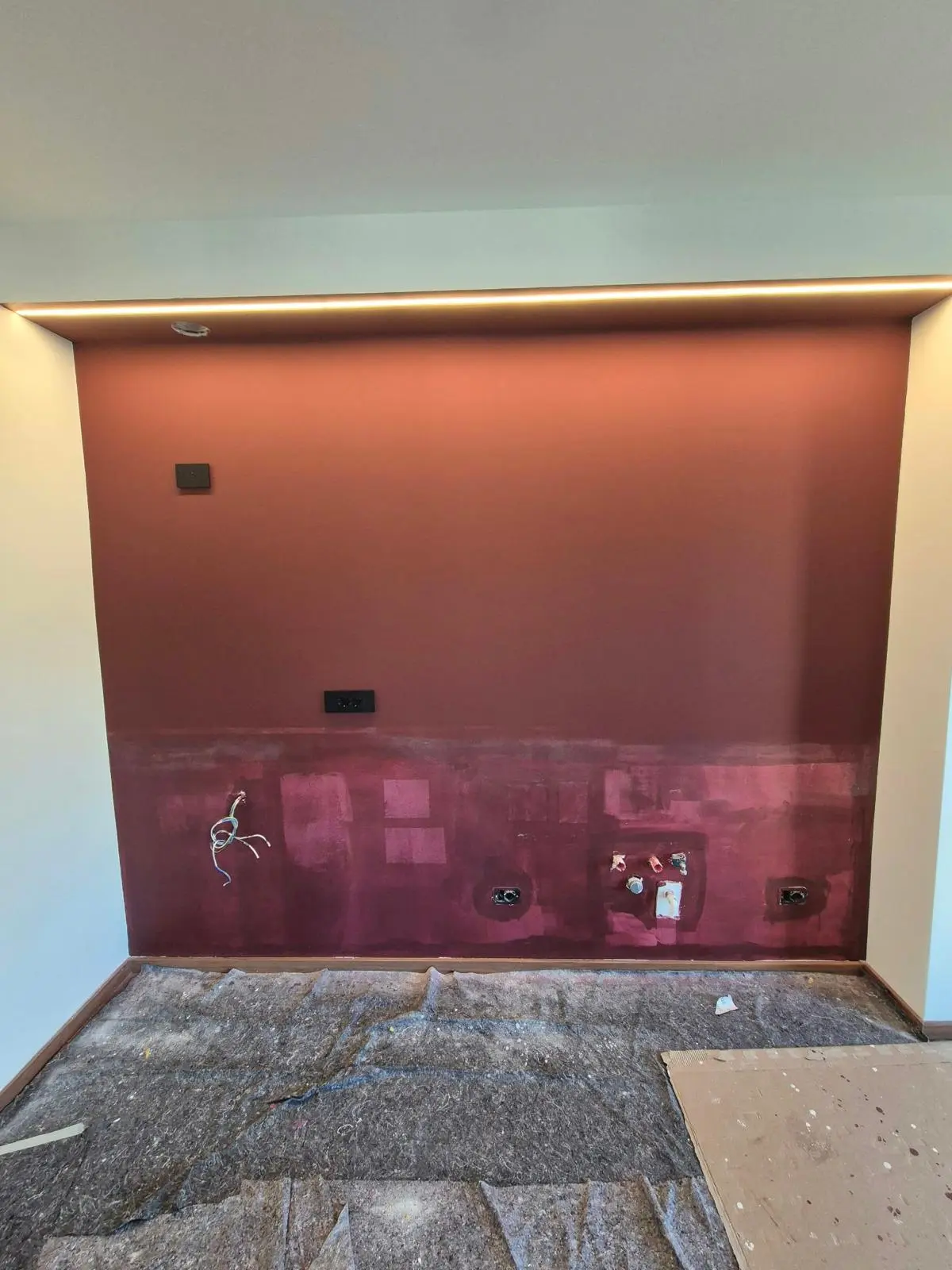 Parete bordeaux in ristrutturazione con prese, cavi e striscia LED accesa sotto il soffitto.