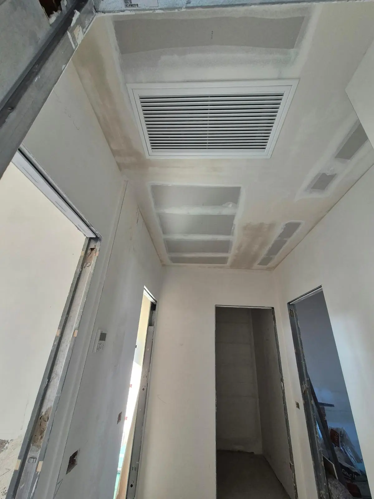 Corridoio in ristrutturazione con controsoffitto in cartongesso e grande griglia di ventilazione.