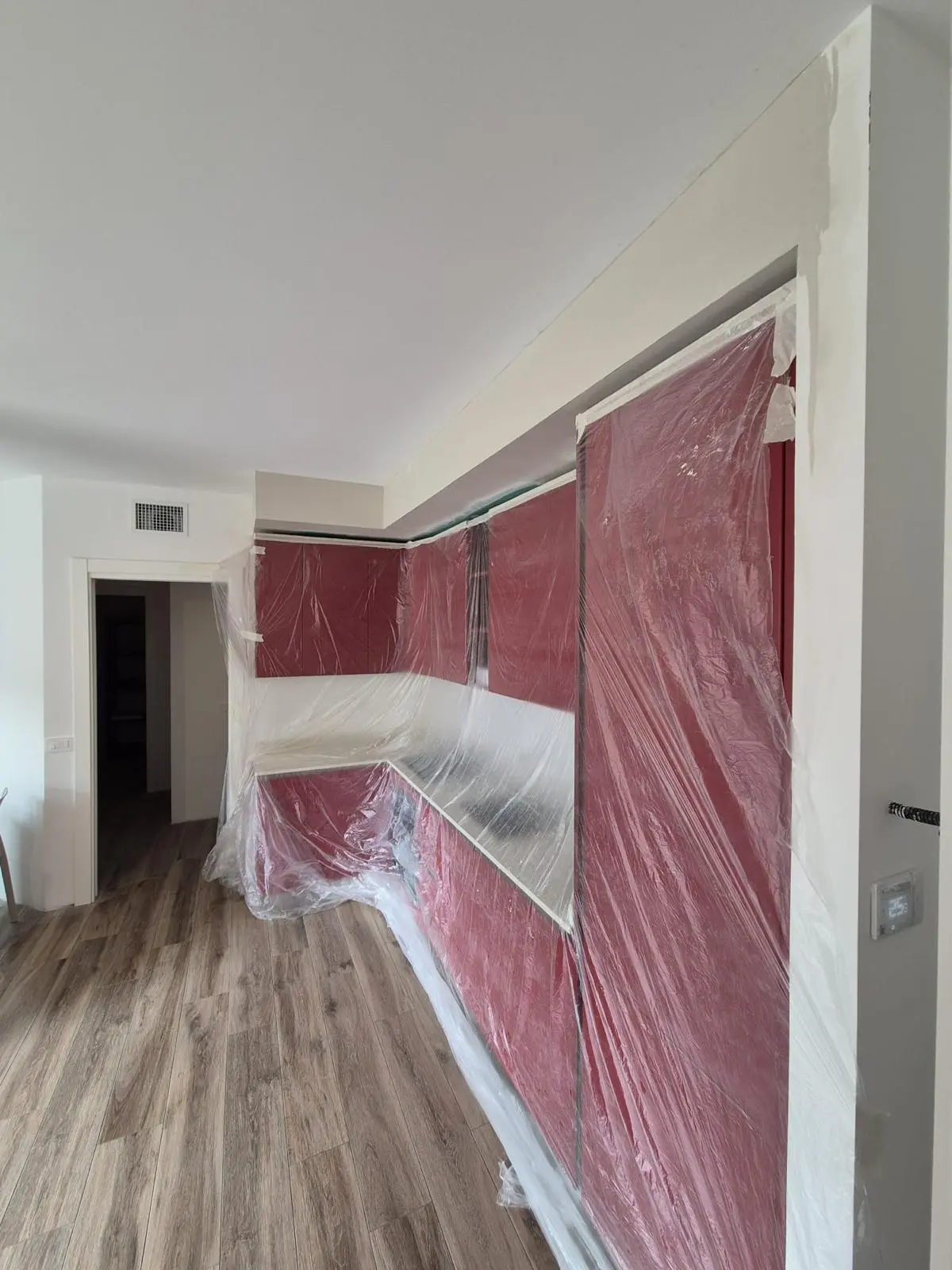 Cucina rossa con pensili, basi e piano di lavoro protetti da teli trasparenti durante i lavori.