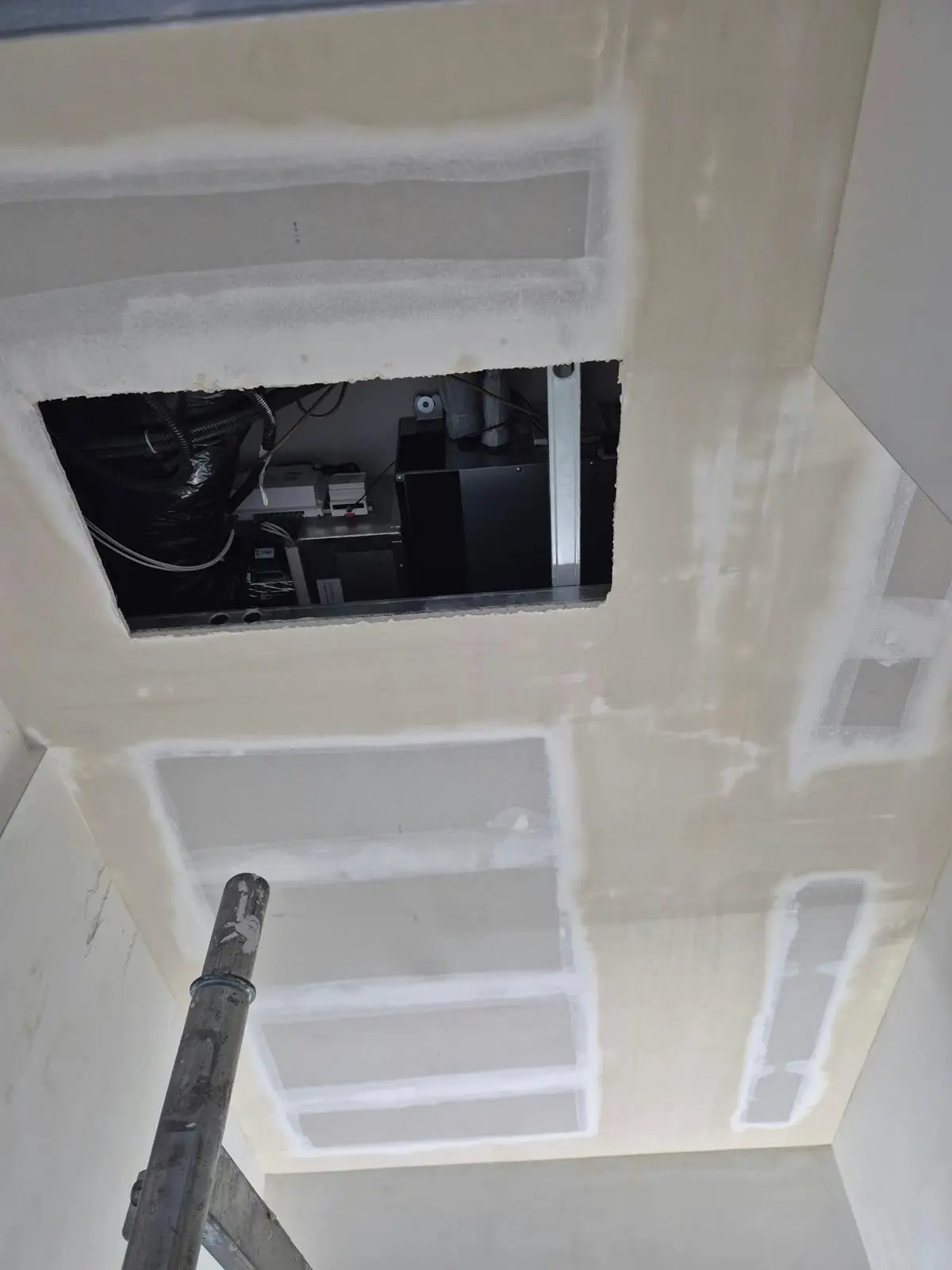 Controsoffitto in cartongesso in lavorazione, con botola aperta su impianti e palo da ponteggio.