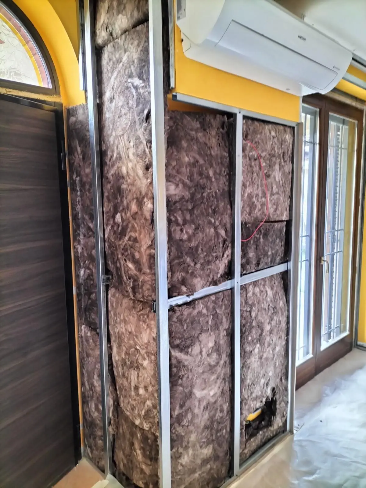 Parete interna in ristrutturazione con isolante in fibra, montanti metallici e condizionatore.