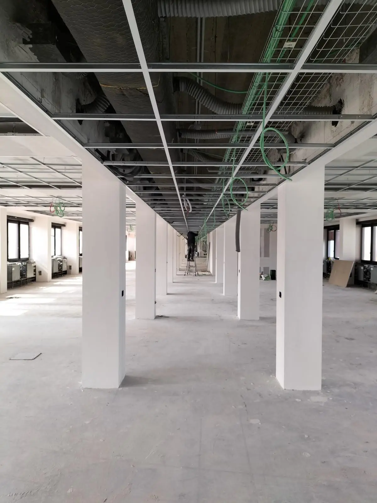 Ampio interno in ristrutturazione con controsoffitto aperto, cavi sospesi e materiali edili impilati.