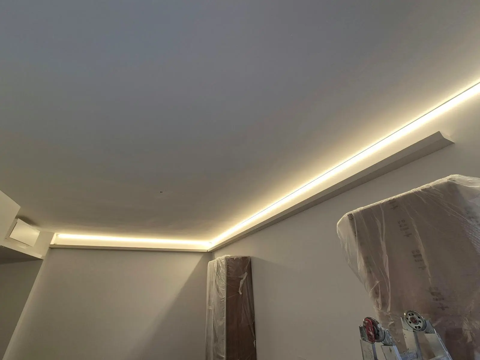 Illuminazione LED perimetrale incassata nel soffitto, con scala e pannelli protetti durante i lavori.