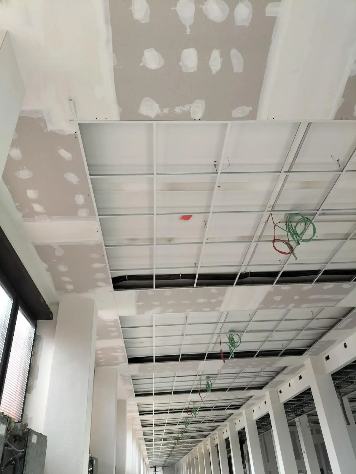 Controsoffitto in costruzione con griglia metallica, pannelli in cartongesso e cavi sospesi lungo un corridoio.
