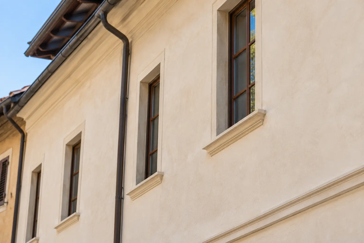 Facciata restaurata con intonaco chiaro, finestre in legno, cornici in pietra e grondaie.