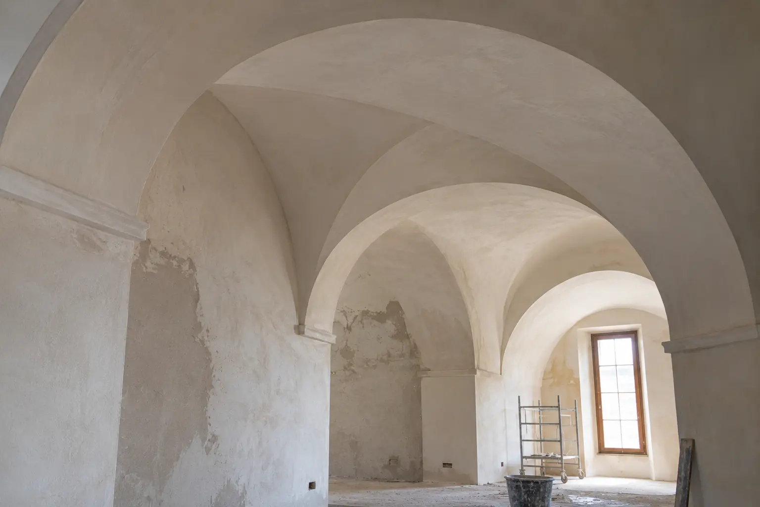 Interno storico con volte a crociera, pareti con intonaco rovinato e ponteggio per il restauro.