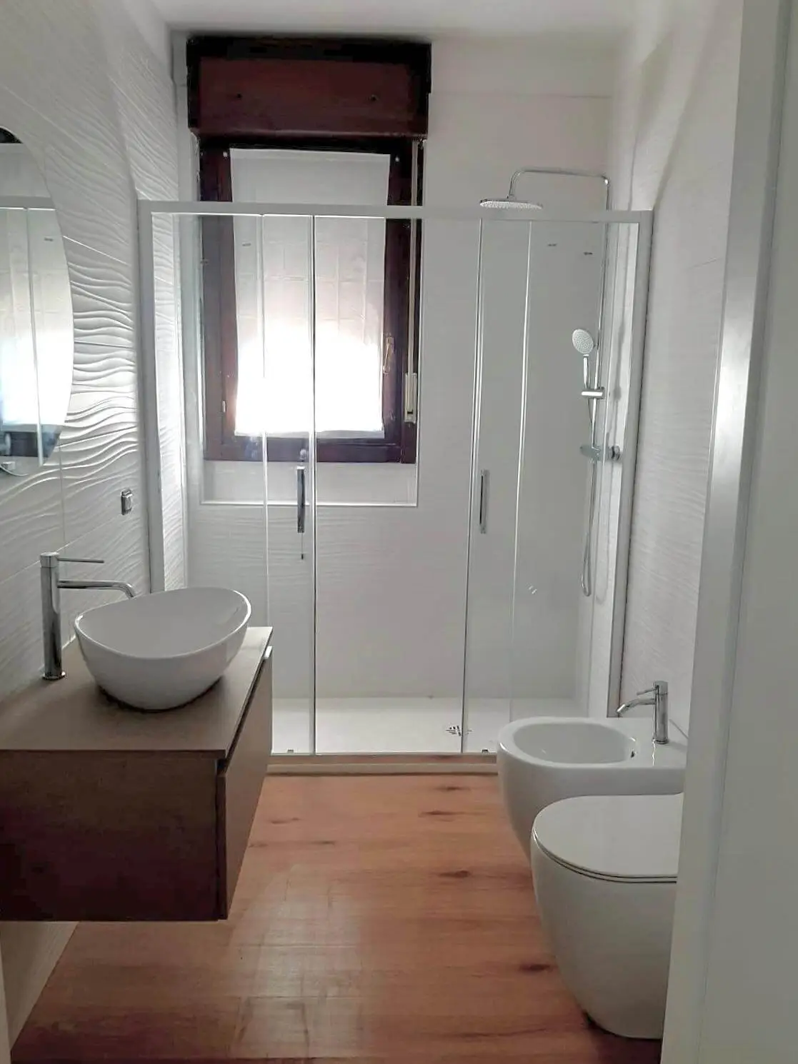 Bagno ristrutturato con doccia in vetro e pavimento effetto legno da Maestro Edilizia | Ristrutturazione Casa a Milano.