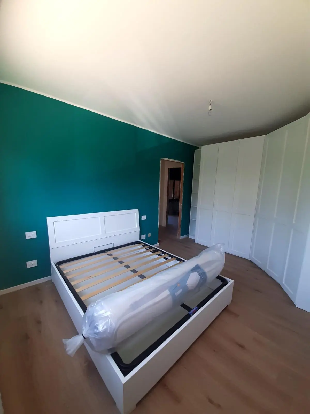 Camera ristrutturata con parete verde, letto e armadi bianchi di Maestro Edilizia | Ristrutturazione Casa a Milano.