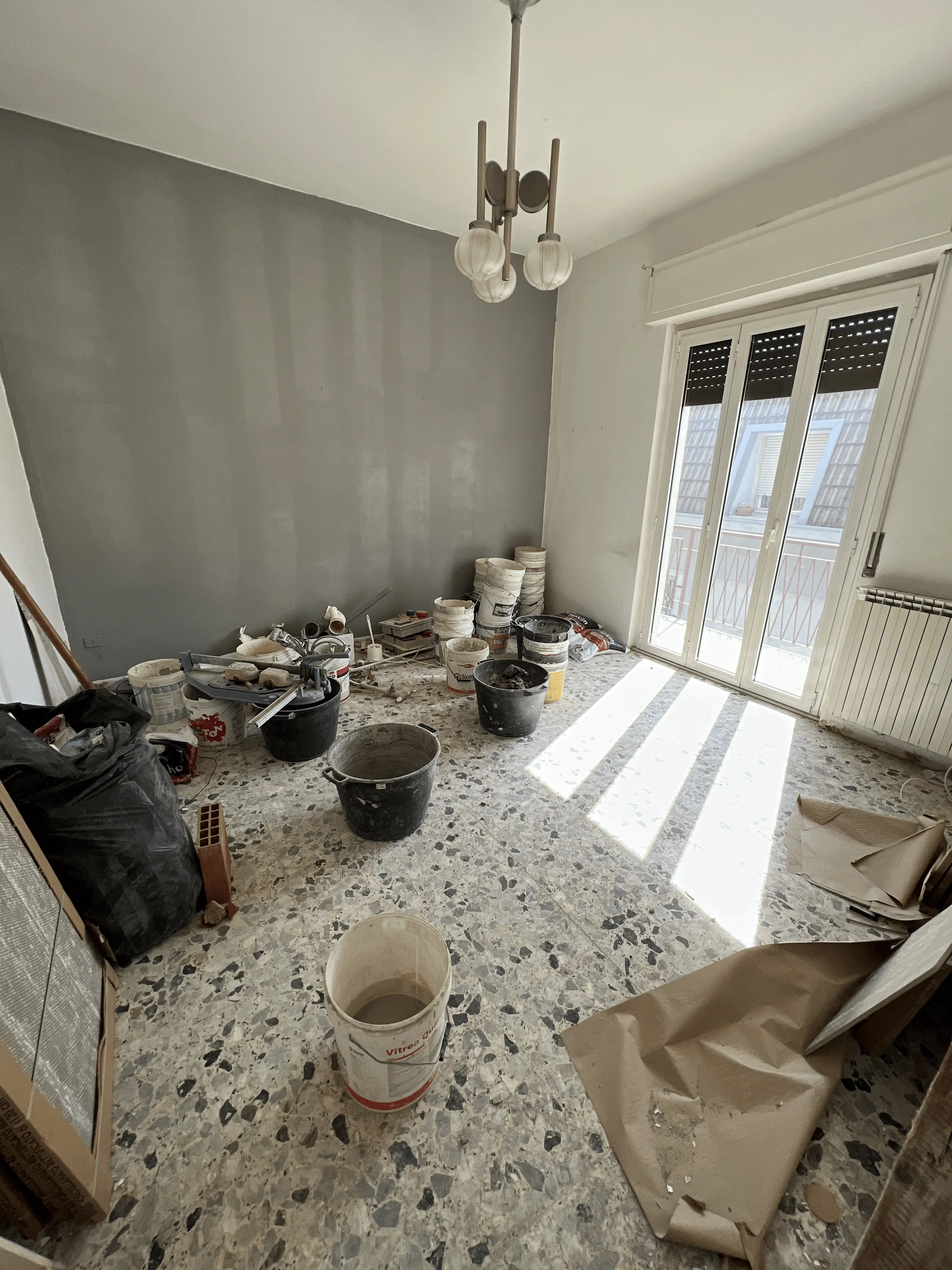 Parete grigia in tinteggiatura con secchi e attrezzi di Maestro Edilizia | Ristrutturazione Casa a Milano.