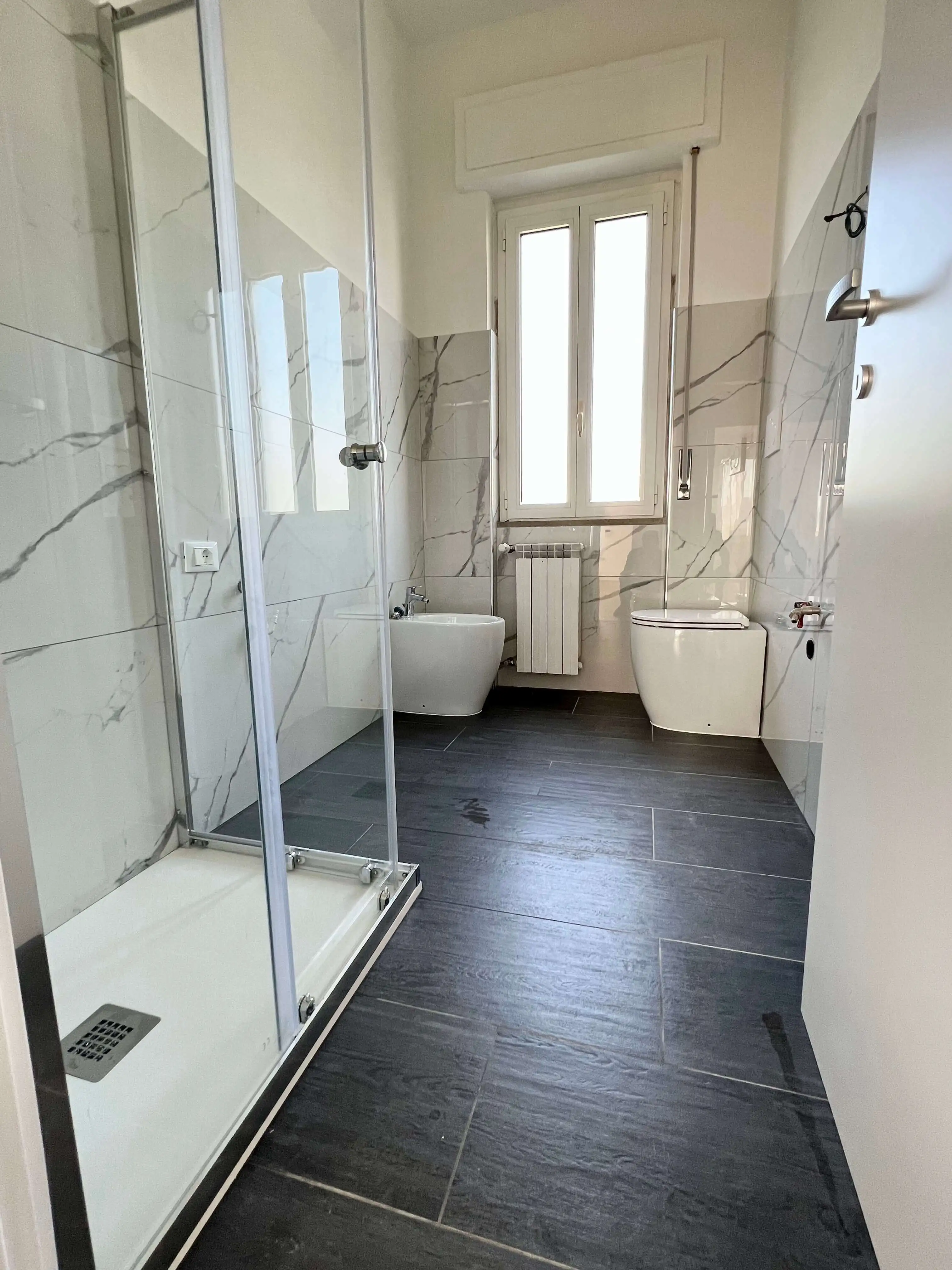 Bagno ristrutturato con doccia in vetro e rivestimenti effetto marmo da Maestro Edilizia | Ristrutturazione Casa a Milano.