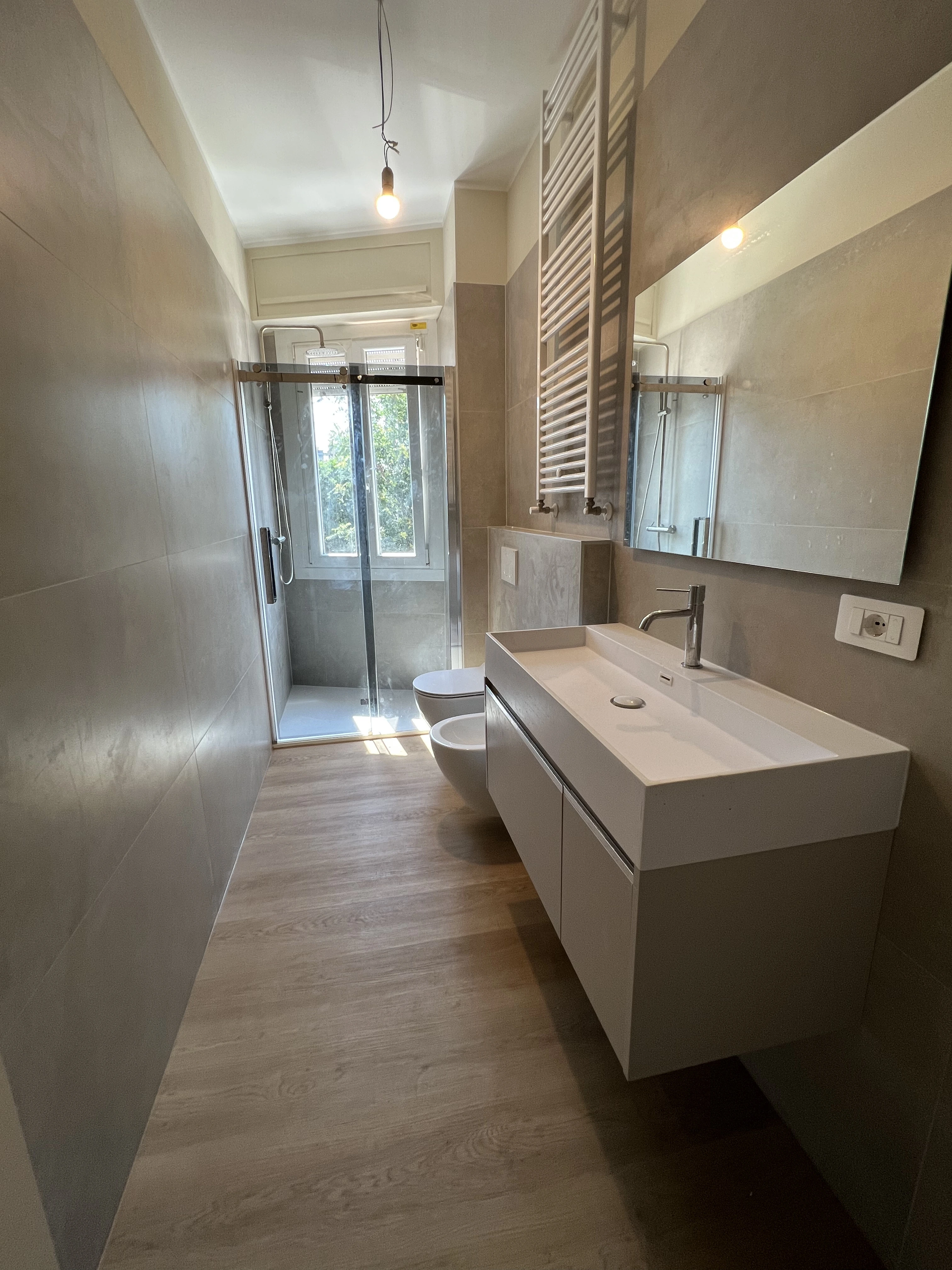 Bagno ristrutturato con doccia in vetro e pavimento effetto legno da Maestro Edilizia | Ristrutturazione Casa a Milano.