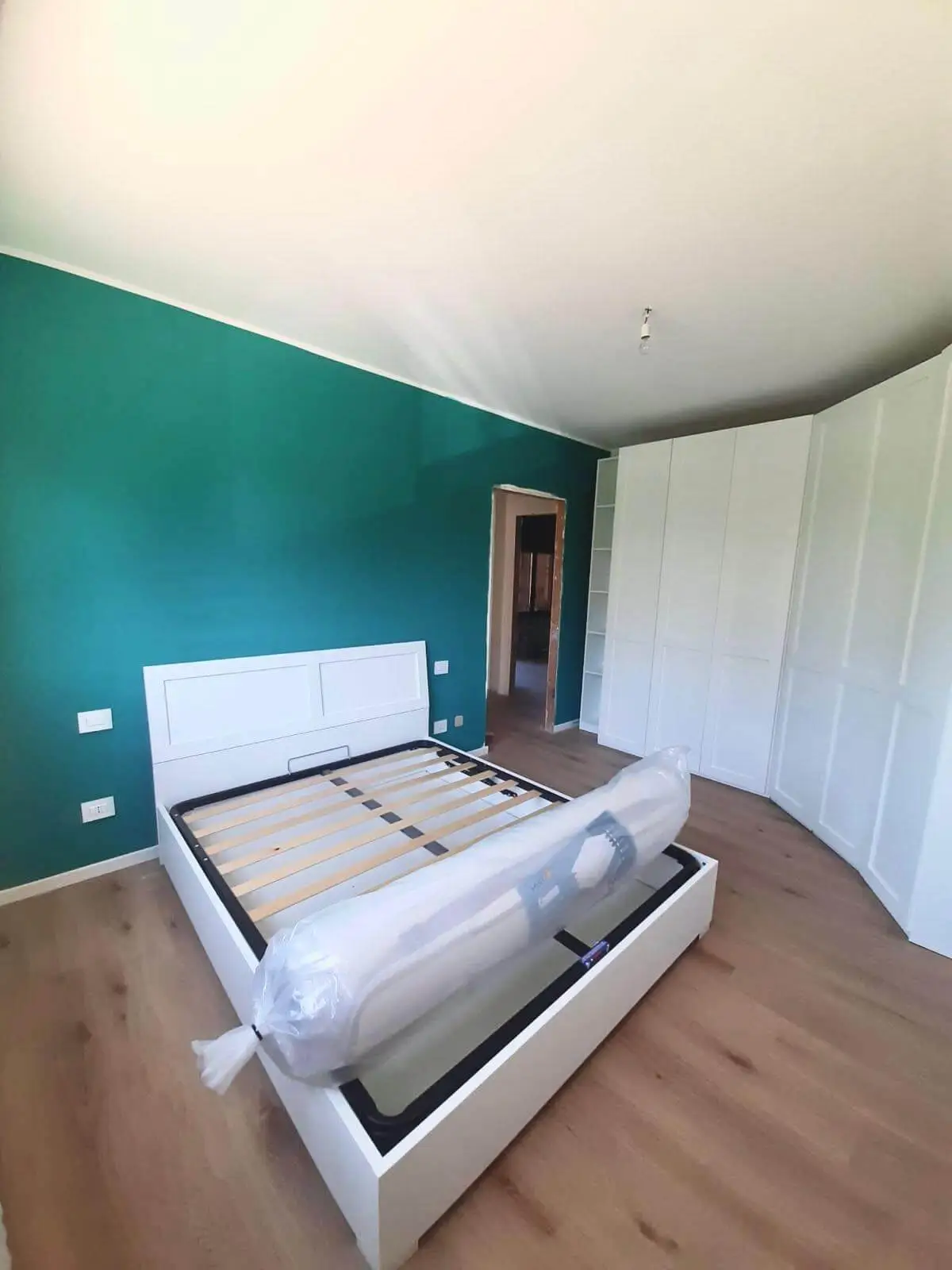 Camera ristrutturata con parete verde, parquet e armadi bianchi da Maestro Edilizia a Milano.